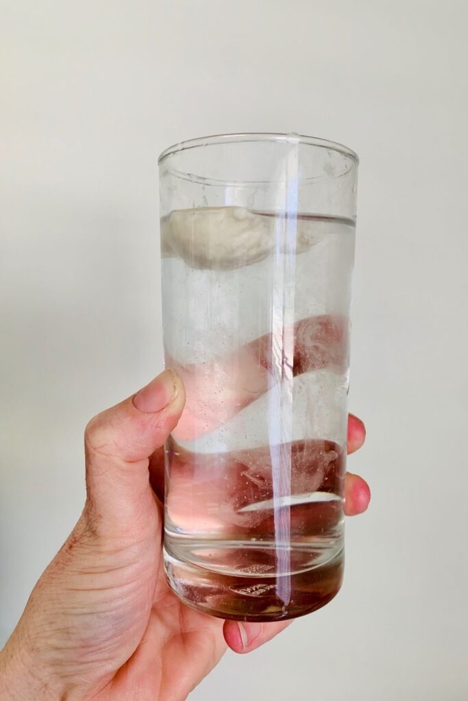 Sourdough float test - hand holding glass of water with a spoonful of sourdough starter floating on top