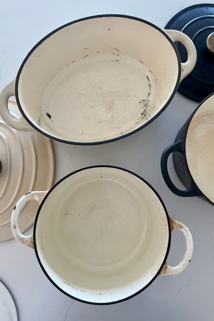 An oval enamel Dutch Oven and a round enamel Dutch Oven both with their lids off. You can see the inside of the pots.