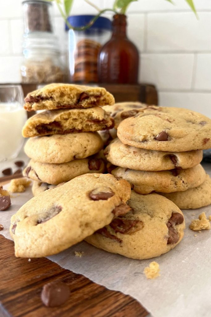 Pile of sourdough chocolate chip cookies. Some of the cookies at the back are broken in half so you can see the soft and chewy texture.