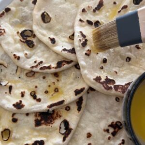 Brush cooked sourdough discard naan bread with melted butter