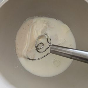 A bowl with the liquid ingredients and dough whisk.