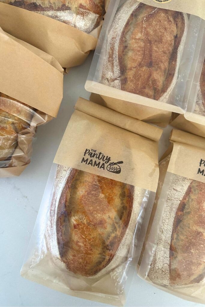 4 small loaves of sourdough bread packaged in paper and plastic bags ready to be sold.