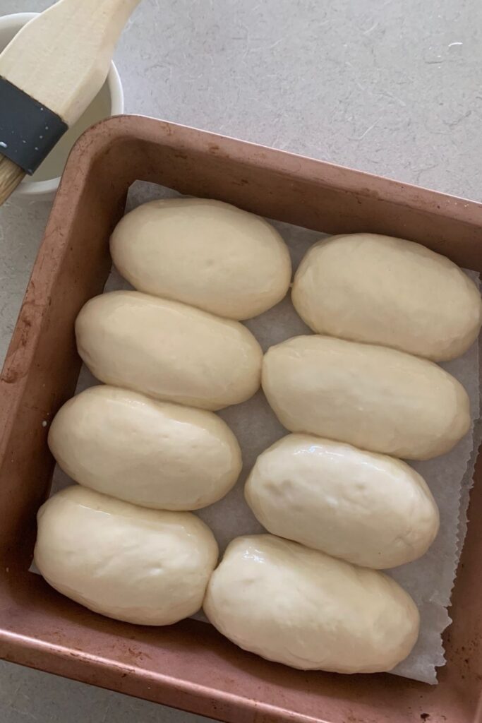 Mini sourdough hot dog rolls proving in a rose gold tin.