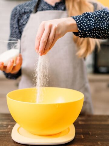 GIRL ADDING SUGAR TO SOURDOUGH BREAD BEING MIXED IN YELLOW BOWL