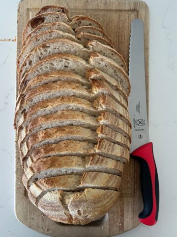 Best Bread Knife for Sourdough Bread - red handled Mercer Bread Knife sitting next to a loaf of perfectly sliced sourdough bread.