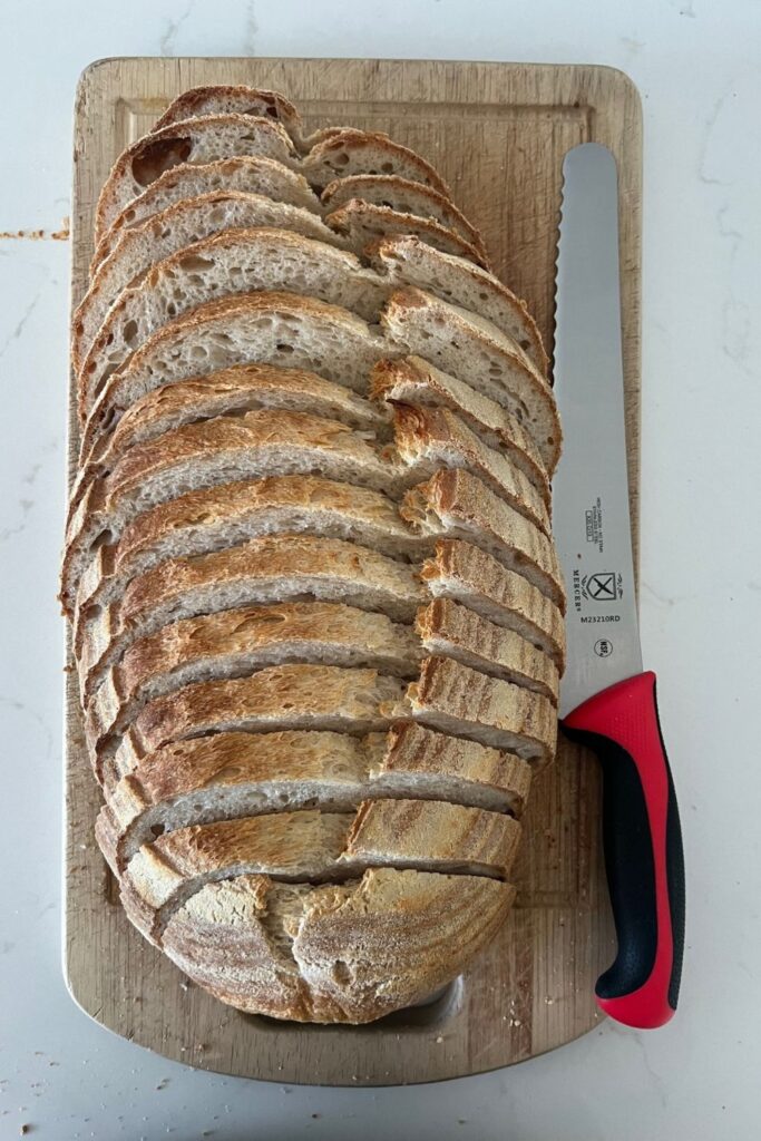 Best Bread Knife for Sourdough Bread - red handled Mercer Bread Knife sitting next to a loaf of perfectly sliced sourdough bread.