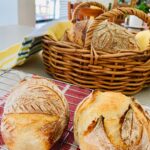 Mini sourdough boules or crusty sourdough rolls sitting on a teatowel and in a basket