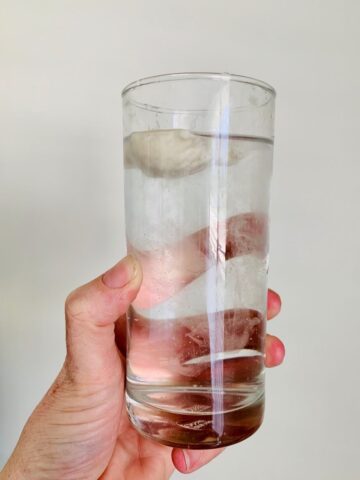 Sourdough float test - hand holding a glass of water with a spoonful of sourdough starter floating on top of the water