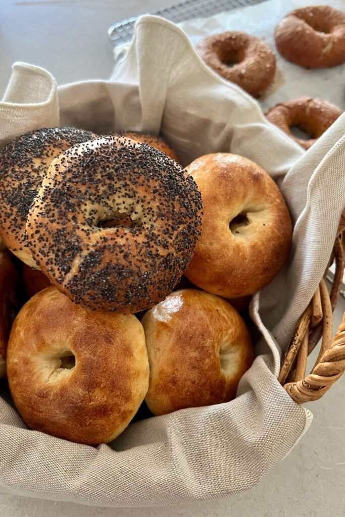 Sourdough egg bagels arranged in a cane basket with a beige linen napkin.