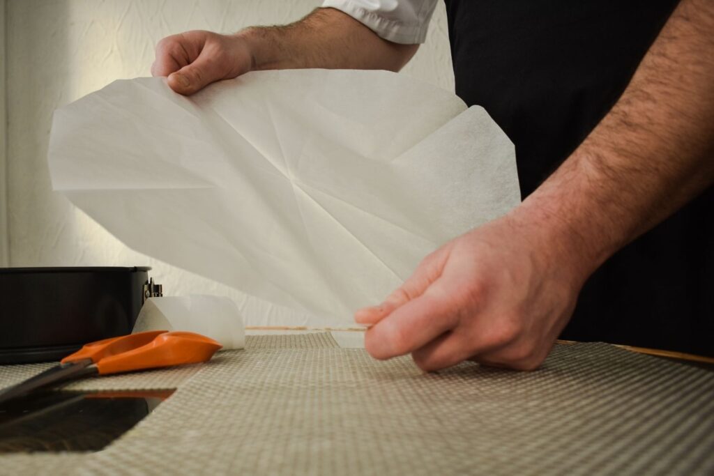 Best alternatives to parchment paper for sourdough baking - man holding a piece of parchment paper in the shape of a circle. There are orange scissors next to him.