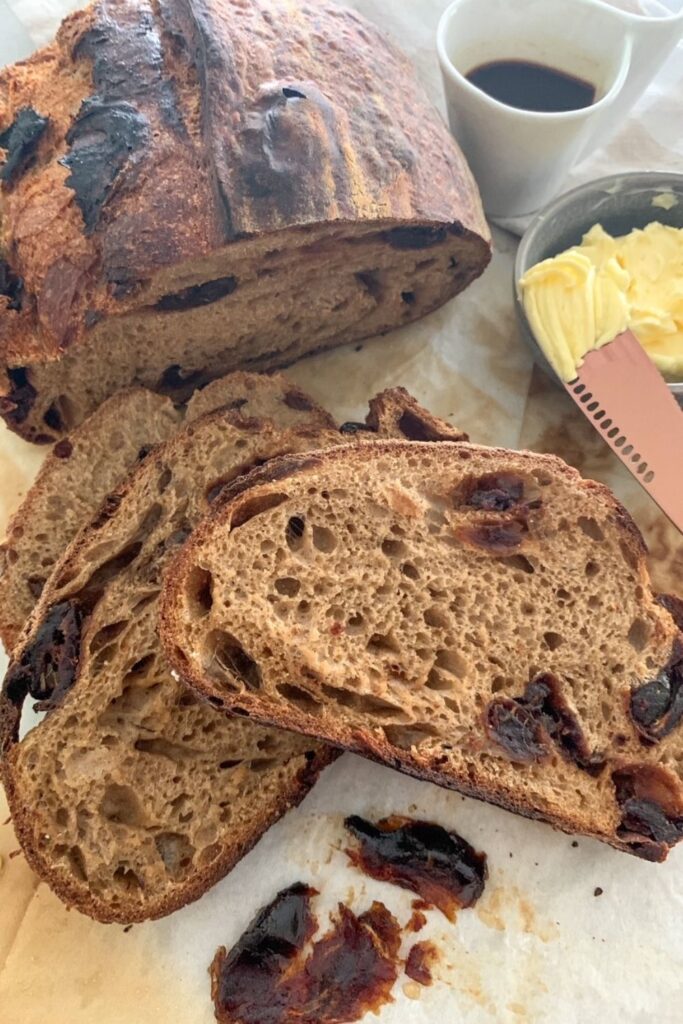 Coffee and maple infused date sourdough bread that has been sliced and is sitting next to a bowl of butter. There is a small cup of espresso coffee in the background.