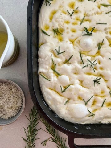 Sourdough focaccia bread recipe - bubbly sourdough focaccia in a black cast iron pan, studded with rosemary and drizzled with olive oil