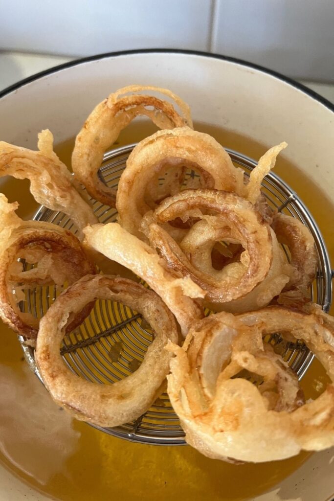 Sourdough onion rings being scooped out of hot oil using a metal spider scoop.