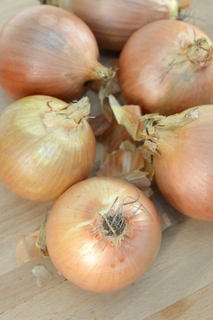 5 yellow onions sitting on a wooden board.