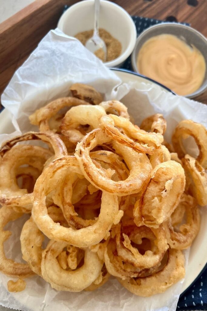 Sourdough onion rings served in a blue rimmed dish along with sriracha mayonnaise and seasoned salt.