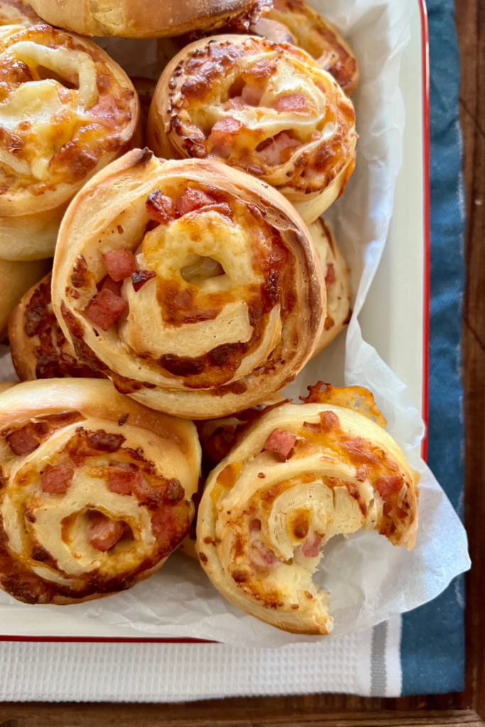 Sourdough pinwheels with ham and cheese piled up - there is one with a bite taken out of it to show the fluffy texture on the inside.