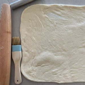 dough rolled out into a rectangle and there is a rolling pin and pastry brush laying next to it
