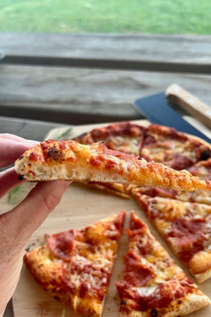 Photo showing a hand holding a slice of pizza to show a perfect crust - it doesn't sag when being held at the edges.