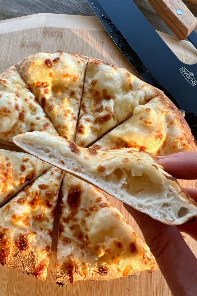 Photo showing a hand holding a slice of pizza to show a perfect crust - it doesn't sag when being held at the edges.