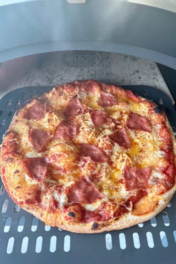 Sourdough pizza being taken out of gas fired pizza oven using a perforated pizza peel.