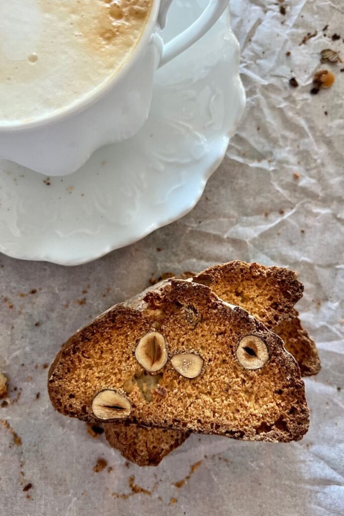 Sourdough biscotti stacked on a white background. There is a coffee cup sitting in the top left corner of the photo.