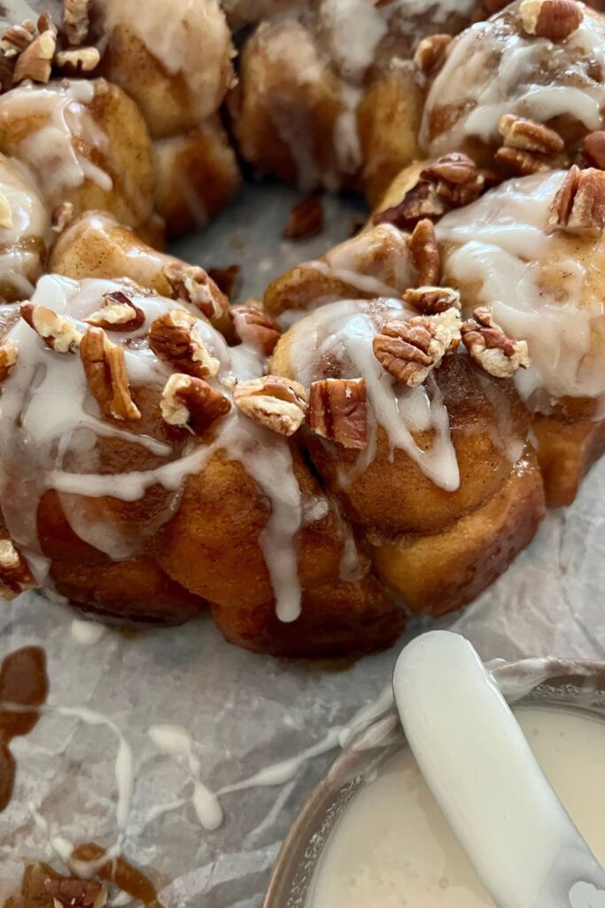 Sourdough discard monkey bread sitting next to a dish of vanilla icing that has been used to drizzle the bread.