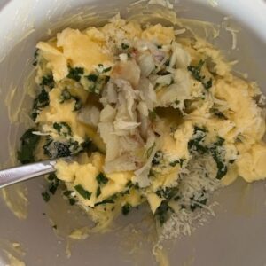 Roasted garlic being mixed in a bowl with butter, salt, parsley and parmesan cheese