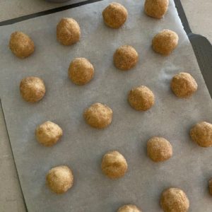 Snickerdoodle cookie dough balls on a cookie sheet lined with baking paper.