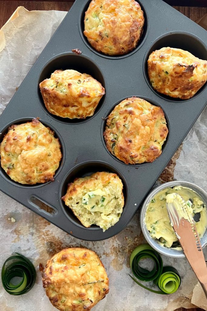 Sourdough zucchini muffins sitting in 6 hole muffin tin alongside a dish of whipped chive butter