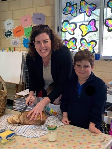 Sourdough for busy moms - easy sourdough recipe for time poor moms - this photo shows a mom and son slicing sourdough bread together with a jar of sourdough starter in front of them.