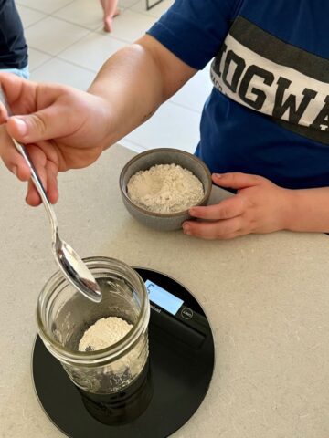 Young child measuring rye flour on a kitchen scale to make a sourdough starter.