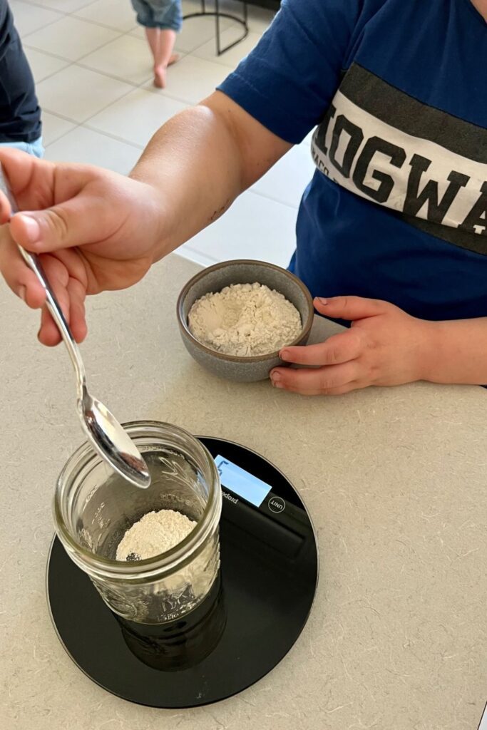 Child weighing flour to create a sourdough starter - how to teach kids to bake sourdough bread