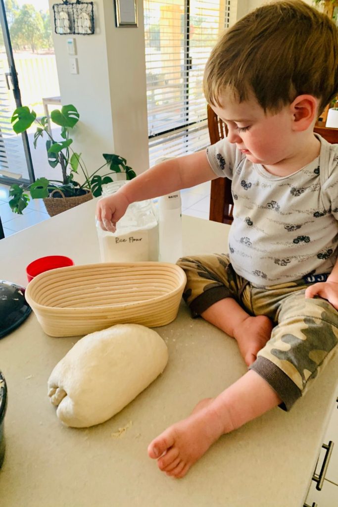 Child sitting on kitchen counter sprinkling rice flour into bannetons.