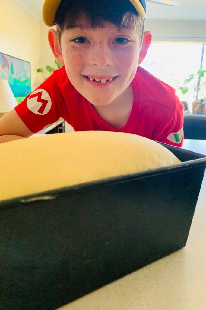 Young boy with a hat watching sourdough bread dough rise in a bread tin