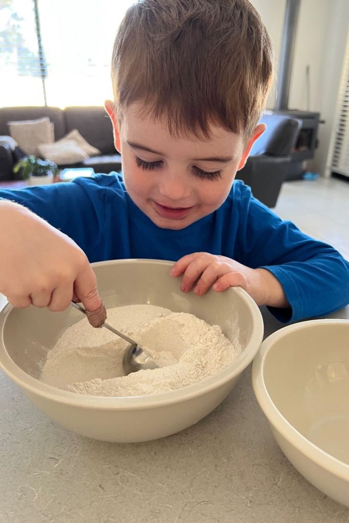 Young child scooping flour using a measuring spoon.