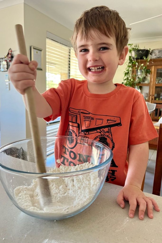Young child stirring sourdough with a wooden spoon.