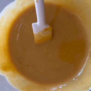 Sourdough starter, pumpkin puree and brown sugar being mixed in a bowl with a white spatula.