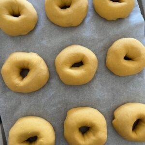 9 sourdough pumpkin bagels getting puffy on a baking tray lined with parchment paper.