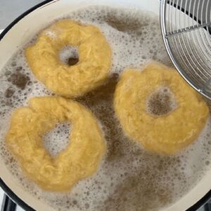 3 pumpkin sourdough bagels being boiled in a pot of honey water