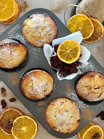 A tray of orange cranberry sourdough muffins decorated with dehydrated orange slices and dusted with powdered sugar.