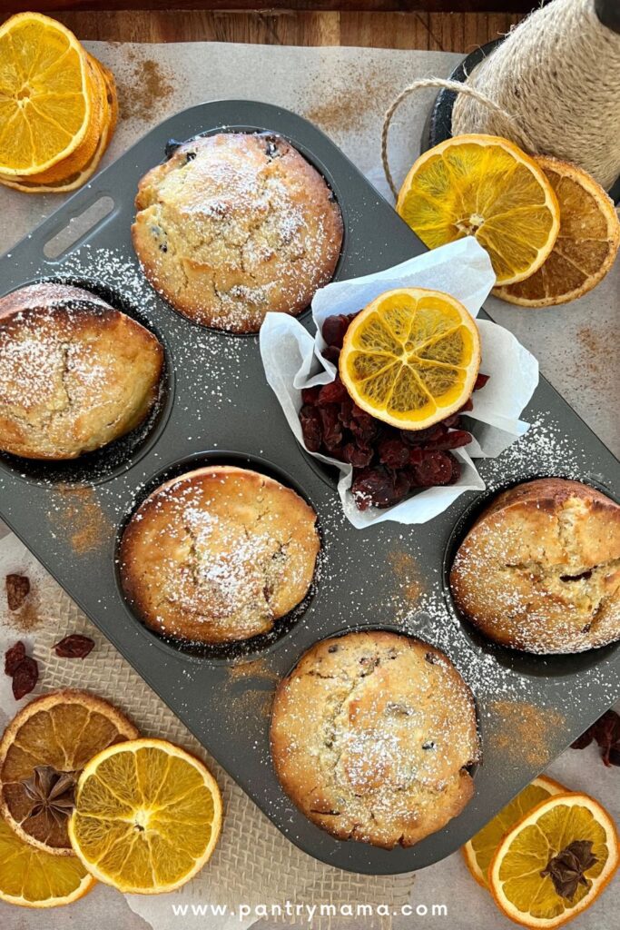 A tray of orange cranberry sourdough muffins decorated with dehydrated orange slices and dusted with powdered sugar.