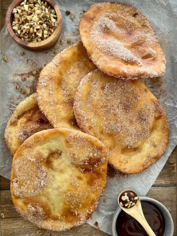 Sourdough Elephant Ears dusted in cinnamon sugar. There is a dish of chocolate sauce and crushed walnuts in the picture too.