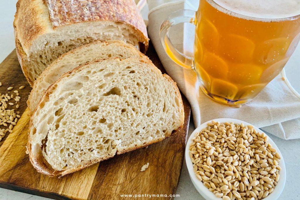 sourdough bread made with home brewed beer - the picture shows the sliced sourdough, a glass of beer and a bowl of wheat berries.