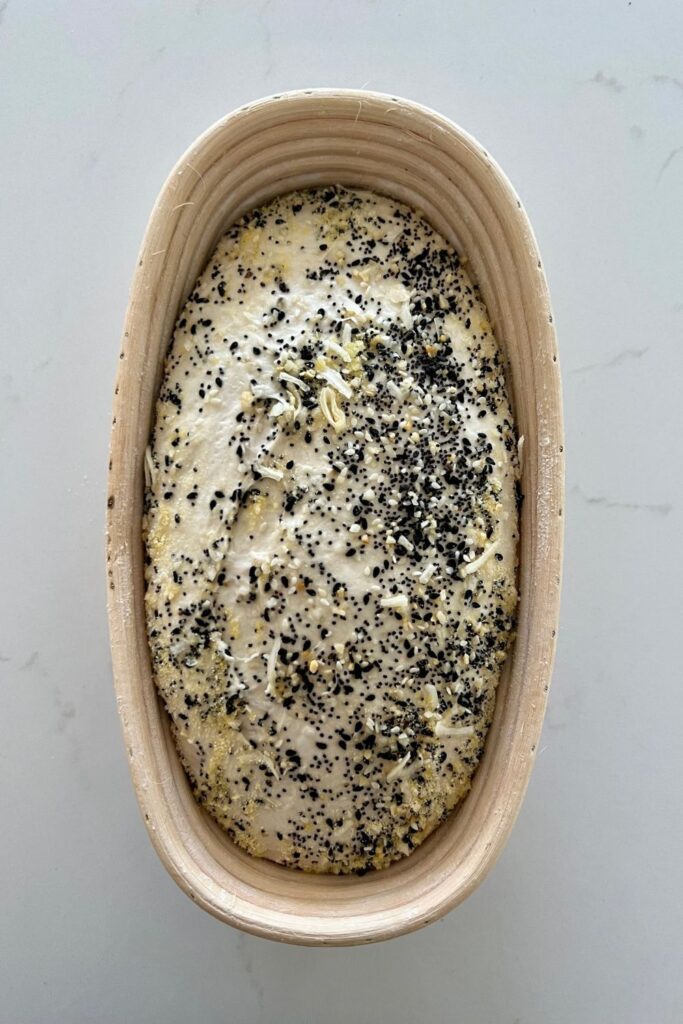 Sourdough bread dough in an oval banneton. The bread has been coated in Everything Bagel Seasoning.