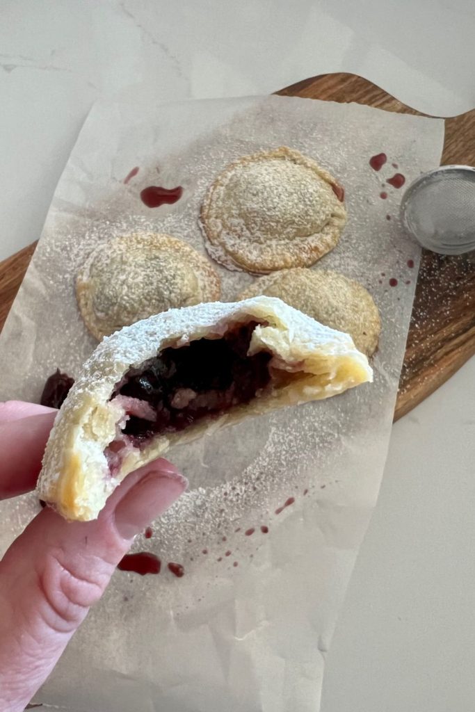 Sourdough pie crust used to make a cherry hand pie. There are 4 hand pies in the photo and one has had a bite taken out of it showing the cherry filling.