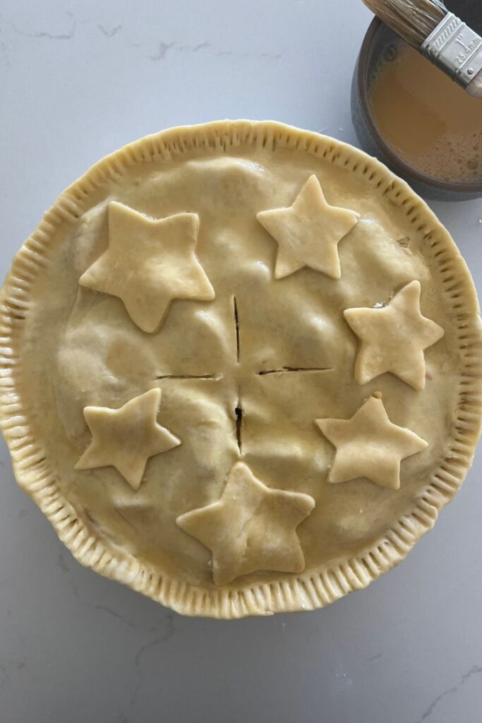 Sourdough pie crust shown unbaked, before it goes into the oven. Starts have been cut out of excess pastry and stuck to the top of the pie crust.