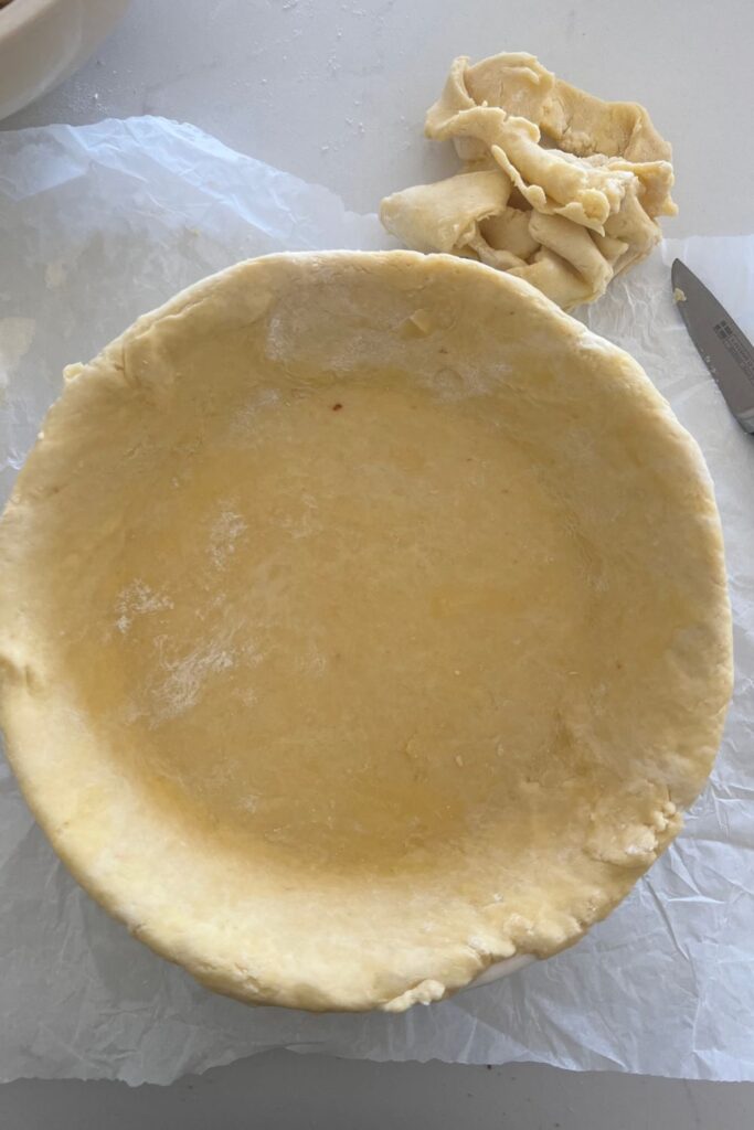 Placing sourdough pie crust into a pie dish and cutting off the excess crust with a small, sharp knife.