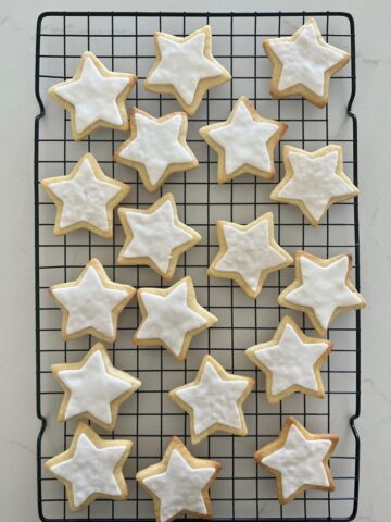 Sourdough sugar cookies decorated with white fondant stars sitting on a black wire rack.