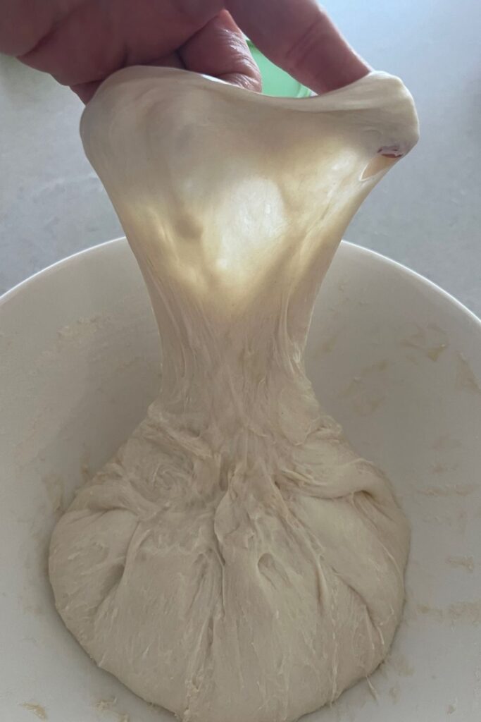 Sourdough window pane being shown - dough being pulled into a thin layer to show the light shining through the back. 