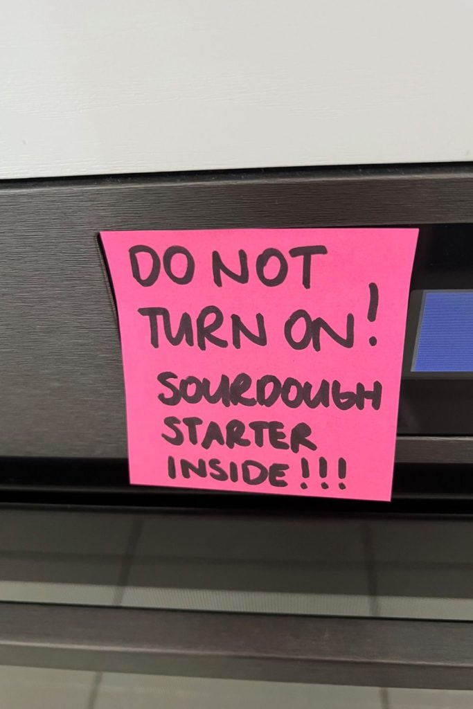 Pink post it note stuck over oven controls. It says "Do Not Turn On - Sourdough Starter Inside"